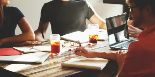 Team collaborating at a table with laptops and drinks, representing the Business Ratings and Reviews Industry.