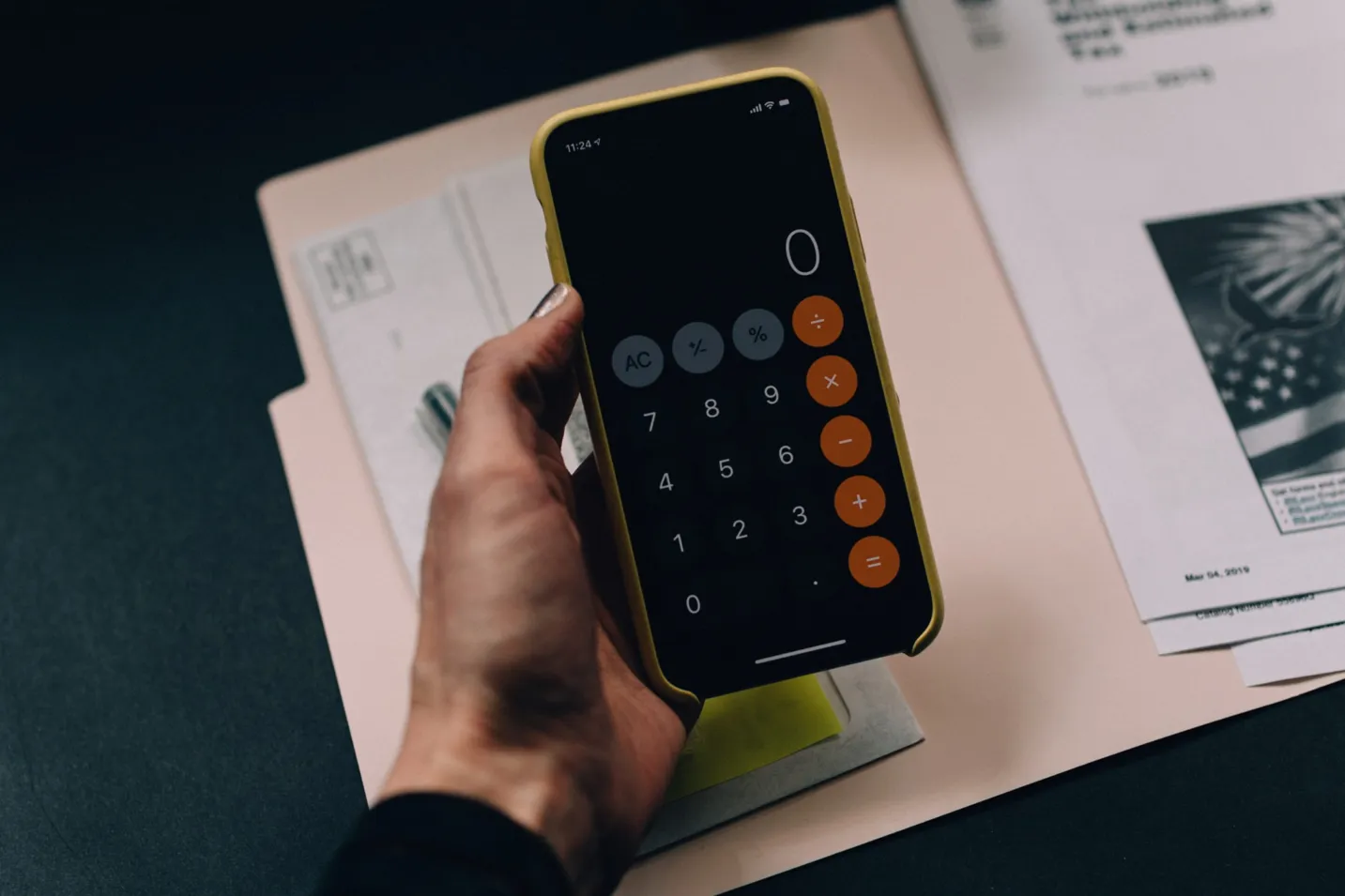 Hand holding a smartphone calculator above documents, symbolizing Shopify pricing calculator
